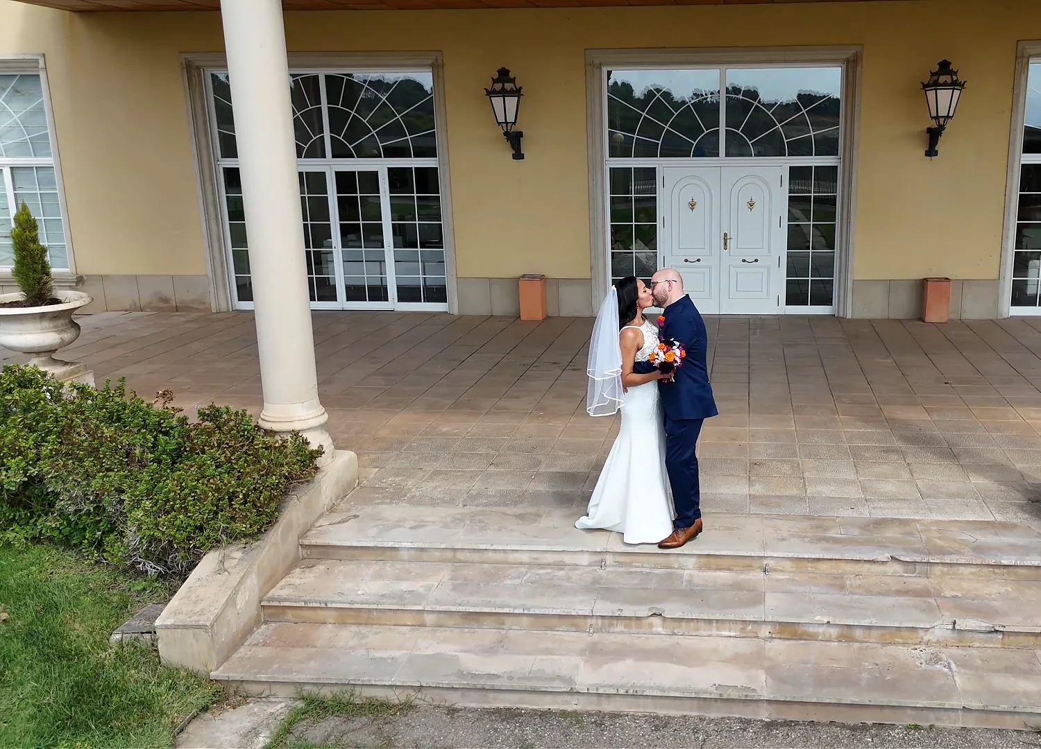 Novios besándose en la escalinata del porche de una masía, vistos desde el dron